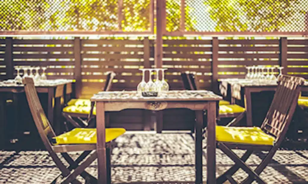 [a wooden table and two chairs with yellow cushions arranged on the outside patio of a restaurant in Uzès]