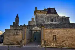 [the entrance of the castle or chateau of the Duchè d'Uzès against a bright blue sky, a medieval roman town of France and a French hidden gem]