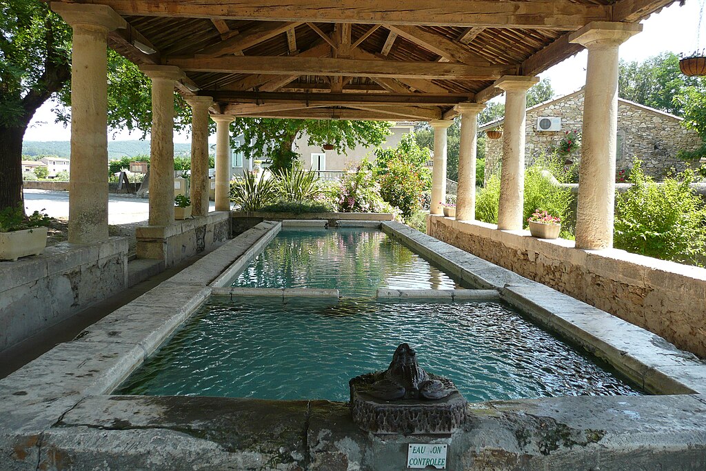 A bronze frog watches over the cement pools of water that form an 18th century French lavoir , a public washing area, in Goudargues, France. The pool is shaded by a graceful portico over slim columns.