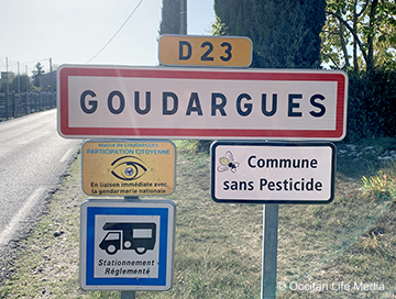 a street side for the town of Goudargues, route D23. Other signs read: Commune Sans Pesticide (Pesticide free community)