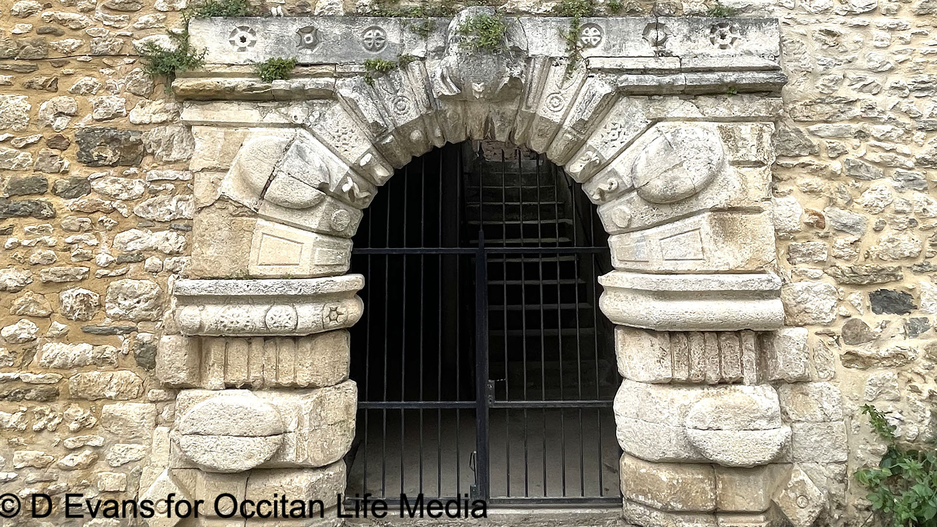 A mysterious archway in Goudargues, France, features geometric patters and carved symbols with a modern gate.